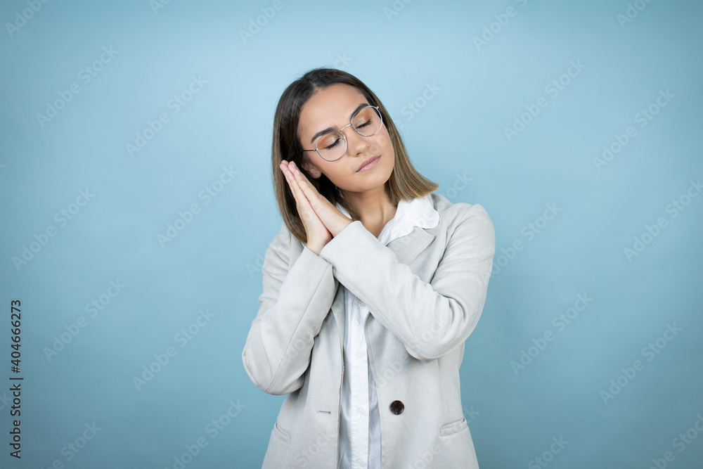 Young business woman over isolated blue background sleeping tired dreaming and posing with hands together while smiling with closed eyes.