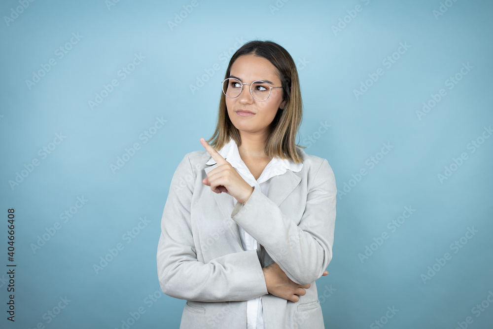 Young business woman over isolated blue background confused and pointing with hand and finger to the side Young business woman over isolated blue background confused and pointing with hand and finger to the side
