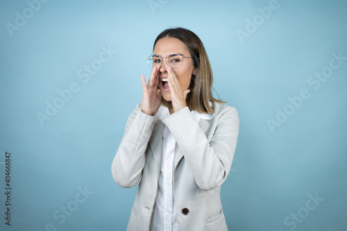 Young business woman over isolated blue background shouting and screaming loud to side with hands on mouth