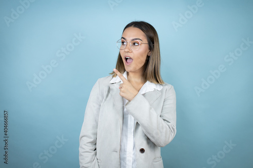 Young business woman over isolated blue background smiling and pointing with hand and finger to the side