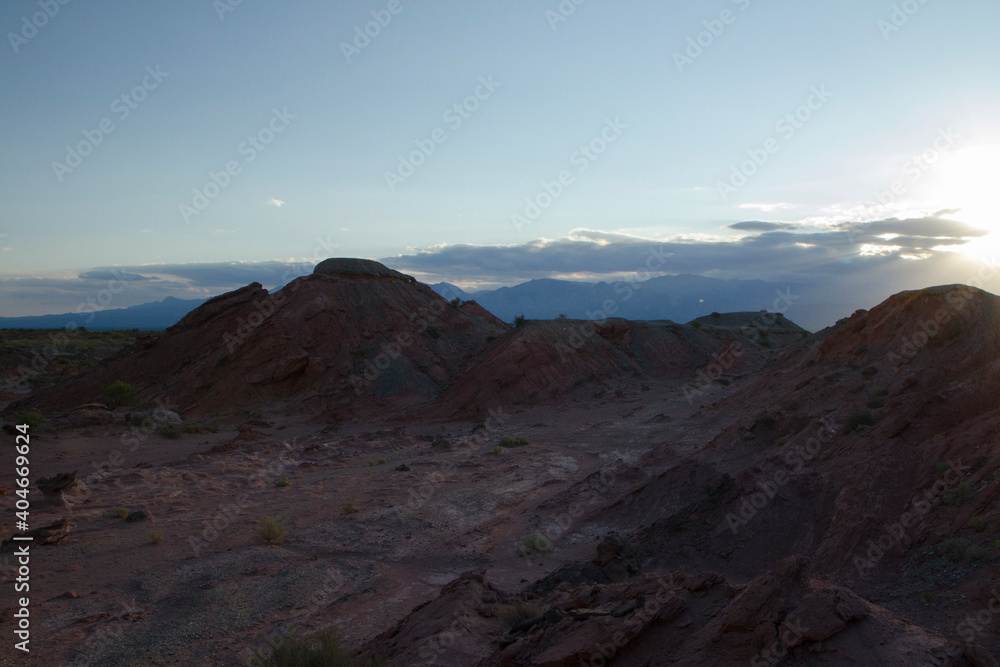 The red canyon and valley at sunset. Panorama view of the arid desert, sandstone formations, rocky mountains, lens flare and hiding sun in Talampaya national park in La Rioja, Argentina.