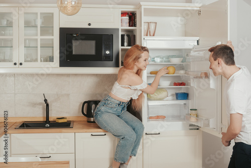 The guy and the girl in the kitchen. Loving couple at home. The woman takes an apple out of the refrigerator. The couple eats healthy food. Useful ration. Prepare breakfast together, morning.