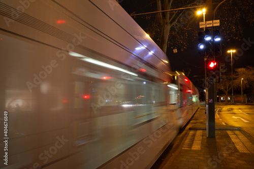 Night view on the sidewalk at intersection beside road and railway track with blur motion of moving light rail tram on the track in Germany.