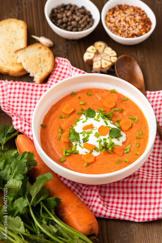Delicious traditional carrot soup with herbs and sour cream on a wooden table.