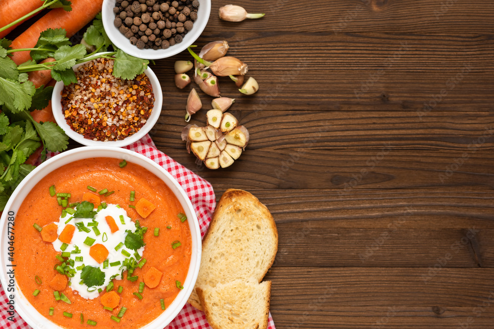 Carrot soup of freshly ground carrots with herbs and sour cream on a wooden background. Carrot soup of freshly ground carrots with herbs and sour cream on a wooden background.