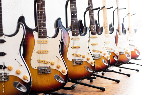 Used and old guitars. Multiple double cutaway solid body guitars on a stand, aligned in a white bright room.