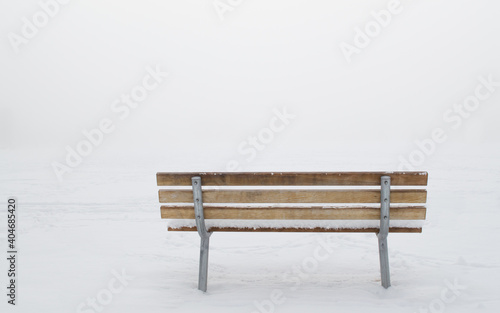 snow covered empty wooden bench viewed from behind in a ghostly winter fog with copy space