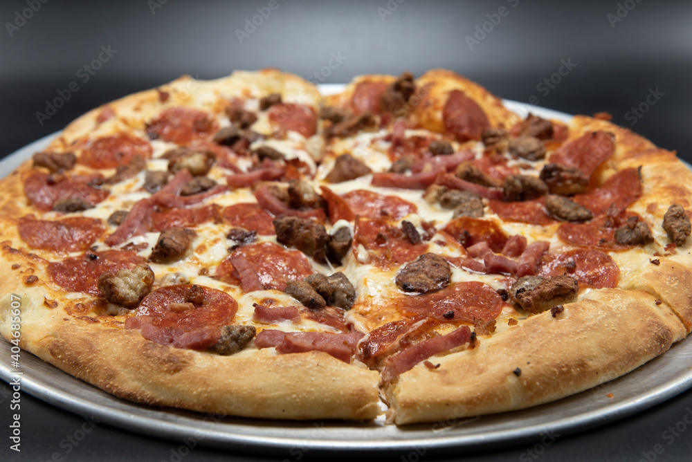 Pepperoni, sausage, bacon, and ham are all the meats that cover this entire pizza.