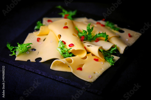 Slices of hard maasdam cheese on a dark background. Cheese with holes.