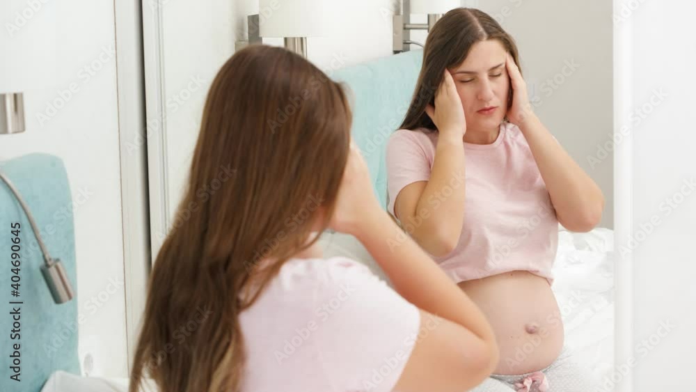 Portrait of pregnant woman suffering from head ache looking in her reflection in mirror. Concept of pregnancy healthcare and medical examination. Portrait of pregnant woman suffering from head ache looking in her reflection in mirror. Concept of pregnancy healthcare and medical examination.