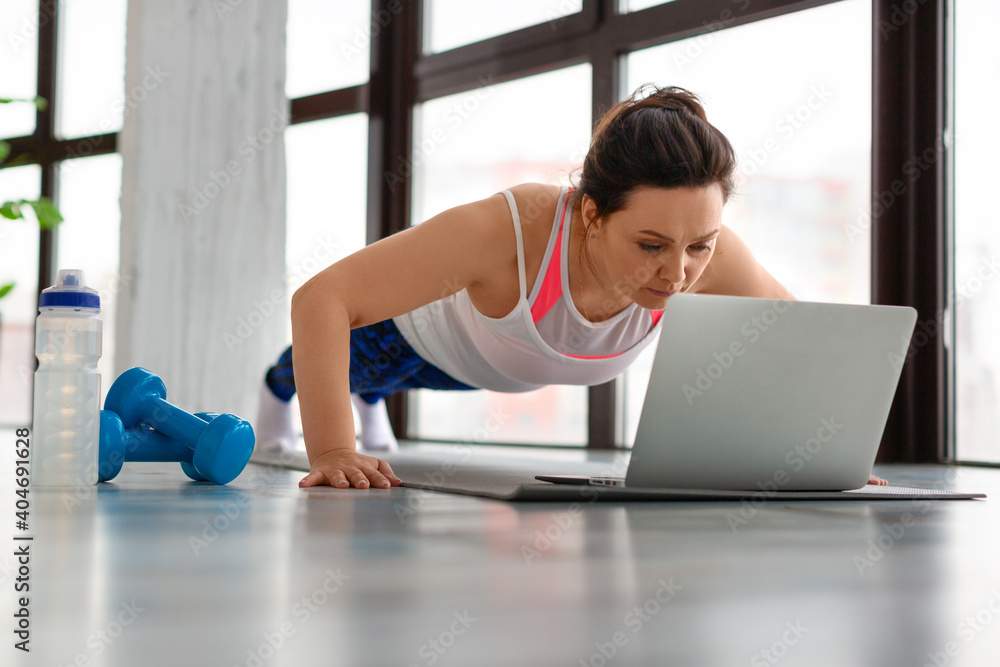 Middle-aged woman doing push-ups at home in front of a laptop monitor. Middle-aged woman doing push-ups at home in front of a laptop monitor.