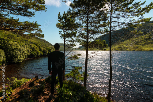 A young man enjoys a view of the Derryveagh Mountains on shores of Lake Veagh in Glenveagh National Park, Church Hill, Letterkenny, Co. Donegal, Ireland