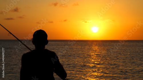 Silhouette of a man fishing in the ocean during a stunning sunset.