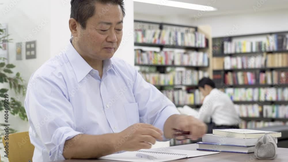 図書館で勉強する中年男性 老眼鏡をかける 図書館で勉強する中年男性 老眼鏡をかける