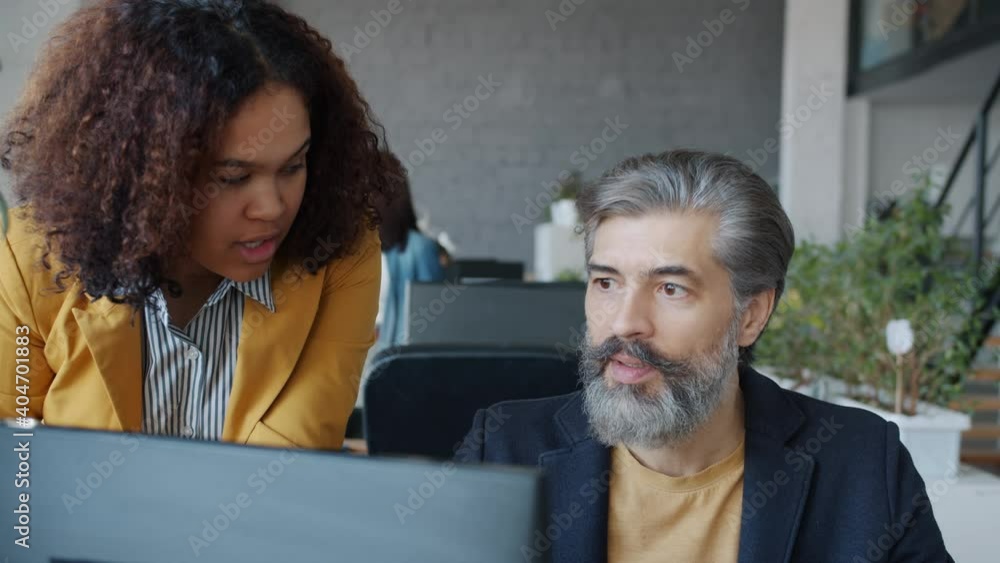 African American woman and Caucasian man are talking using computer looking at screen in shared office. Businesspeople and coworking concept. African American woman and Caucasian man are talking using computer looking at screen in shared office. Businesspeople and coworking concept.