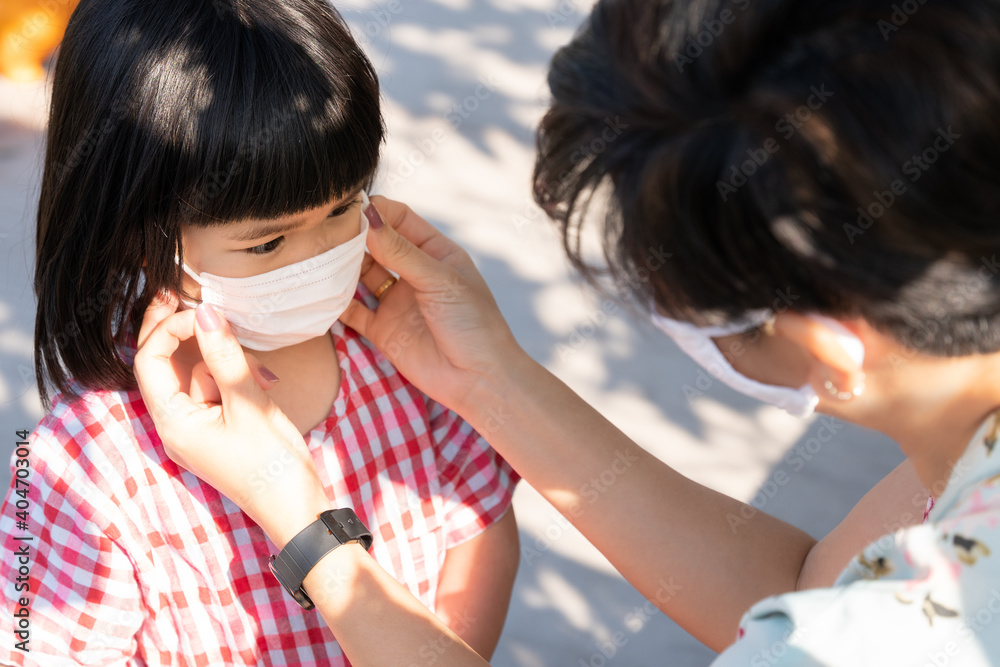 Covid-19 New normal back to school concept. An asian mother put on a children medical face mask for her little girl to preventing coronavirus. Social responsibility, Stop spreading, Stay healthy. Covid-19 New normal back to school concept. An asian mother put on a children medical face mask for her little girl to preventing coronavirus. Social responsibility, Stop spreading, Stay healthy.
