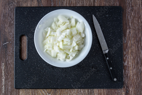 Obraz na plátne Kitchen knife and a diced raw sweet onion on a black cutting board with white bo