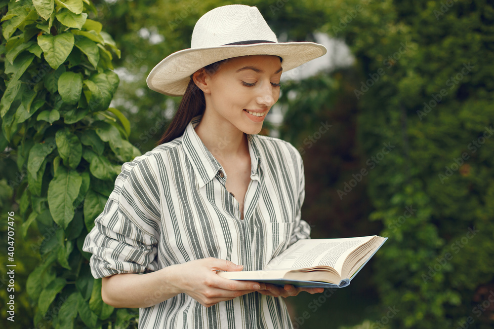 Girl reading book at garden. Nature background. Lady in a hat.