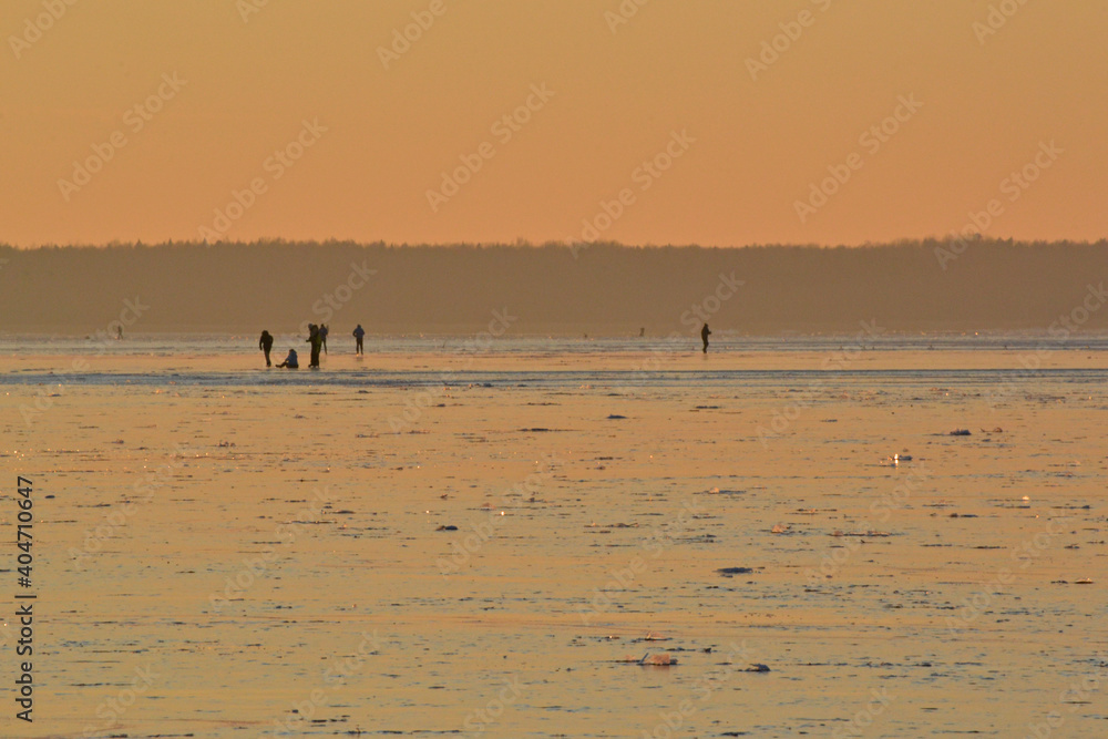 Winter Sea Golden Sunset. People walk on the ice on the snow-covered frozen field of the reservoir.