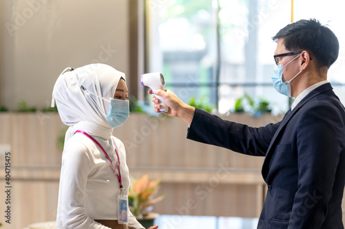Young employees are using a Muslim employee fever meter. Young Man using infrared thermometer. Staff Checking Temperature Using Infrared Thermometer.