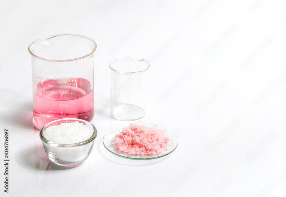 Chemicals for beauty care on white laboratory table. Pink flake chemicals in Chemical Watch Glass, Microcrystalline wax in glass container. Chemicals for beauty care on white laboratory table. Pink flake chemicals in Chemical Watch Glass, Microcrystalline wax in glass container.