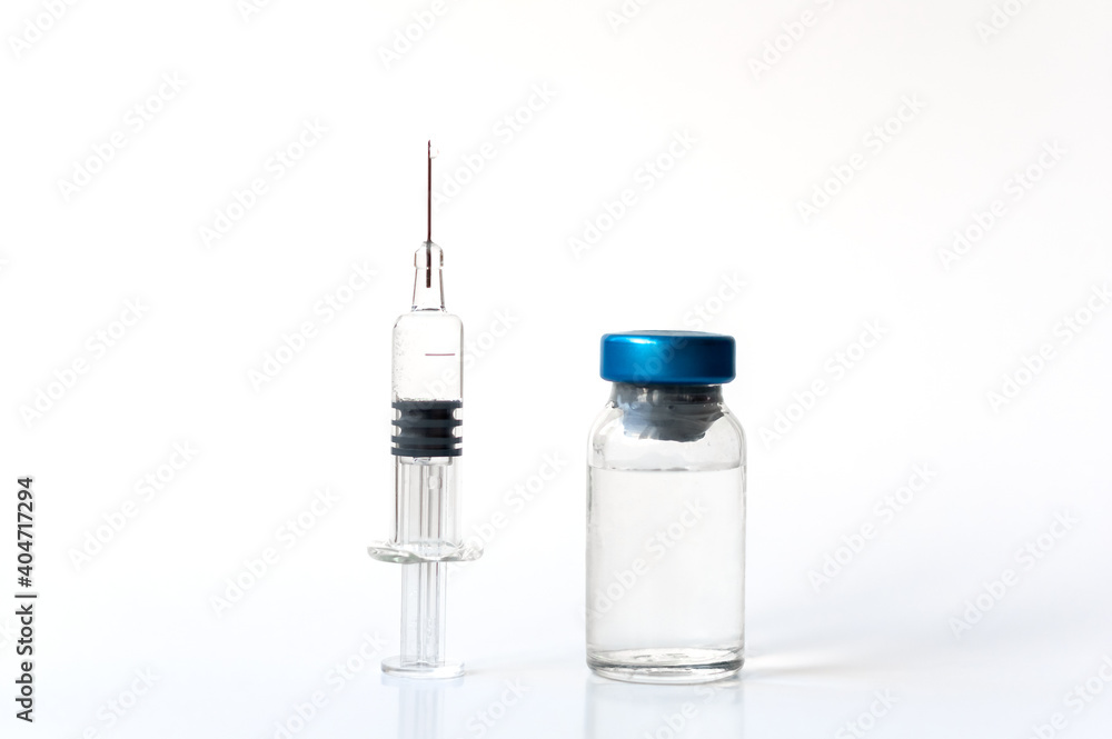 A medical syringe and an ampoule with a medicine on stand on a table on a white background. Serum or vaccine in a syringe with a needle. copy space. A medical syringe and an ampoule with a medicine on stand on a table on a white background. Serum or vaccine in a syringe with a needle. copy space.