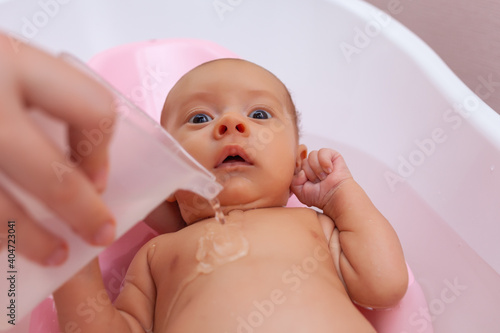 the newborn is bathed in the bathroom, the child is watered with water from a water bucket