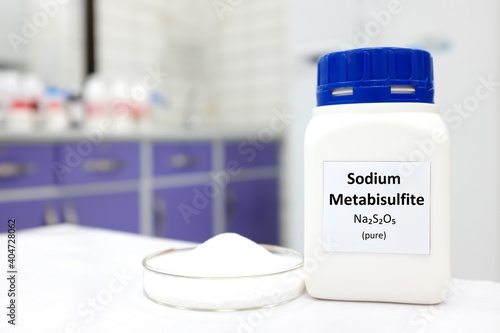 Selective focus of bottle of pure sodium metabisulfite food additive beside a petri dish with white solid powder substance. White laboratory background with copy space. photo