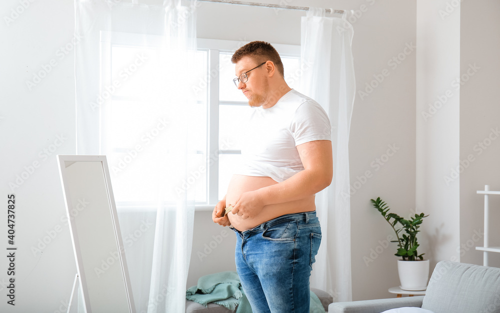 Confused overweight man with measuring tape at home. Weight loss concept