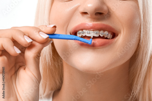 Young woman with dental braces and toothbrush on white background