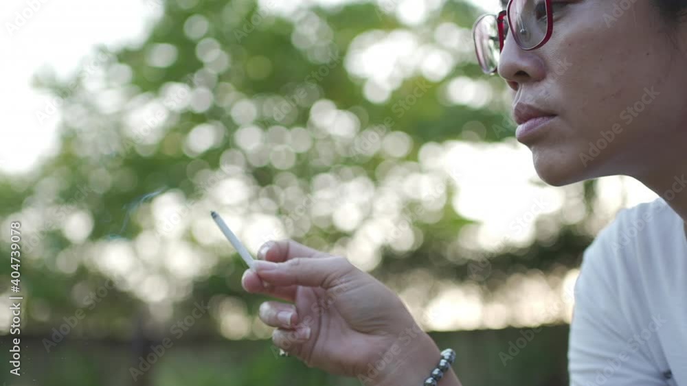Concept of quit smoking and anti cigarette. Asian grey-haired woman smoking a cigarette on Blurred green background Concept of quit smoking and anti cigarette. Asian grey-haired woman smoking a cigarette on Blurred green background