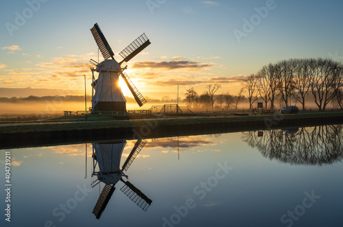 Foggy, winters sunrise at a windmill reflected in a canal.
