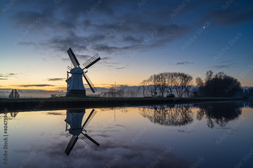 Foggy, winter dawn at a Dutch windmill reflected in a canal.