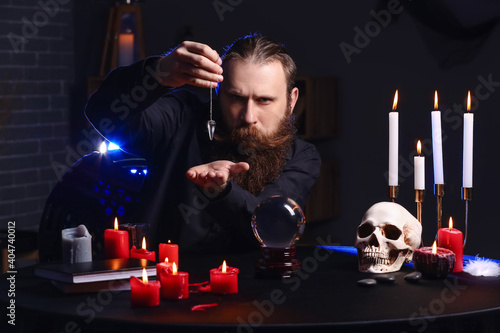 Male fortune teller with pendulum at table