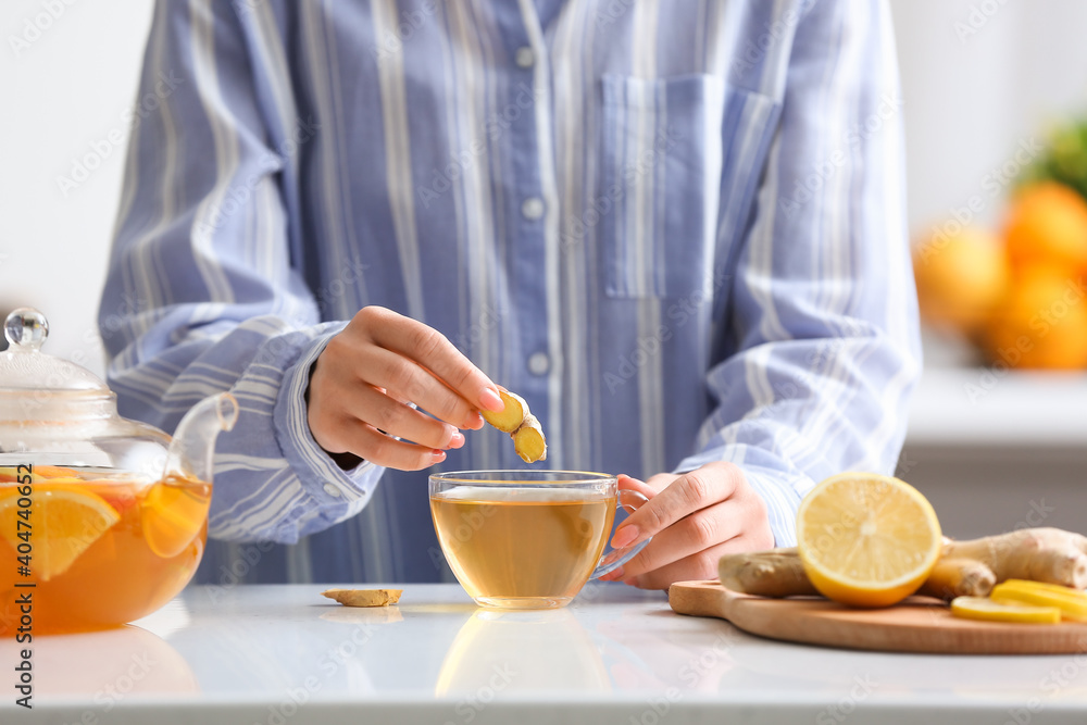 Woman making healthy tea with ginger and lemon in kitchen Woman making healthy tea with ginger and lemon in kitchen