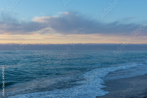 Blue evening serene sea. Calm seascape in azure and pearl shades. Natural background in the twilight. The concept of relaxation and relaxation. Beach with small pebbles, small waves with foam