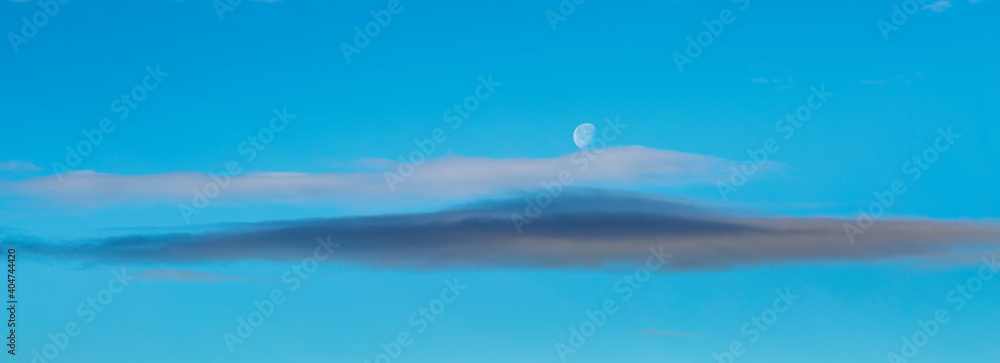 Landscape photograph of the sky with clouds and the crescent moon during the day.