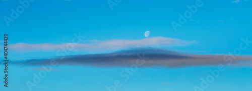 Landscape photograph of the sky with clouds and the crescent moon during the day.