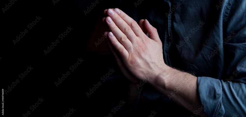 Hands in prayer. The man is praying. On a dark background. Hands out of the dark.