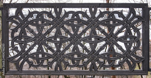 Graceful lattice of the fence with a pattern of oriental ornament in dark color against the background of winter ramtenii branches