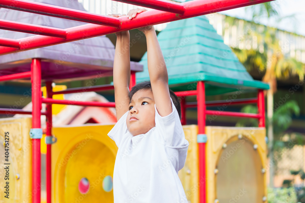 Obraz premium Kid exercise for health and sport concept. Happy Asian student​ child boy playing and hanging from a steel bar at the playground. 6-7 years old.