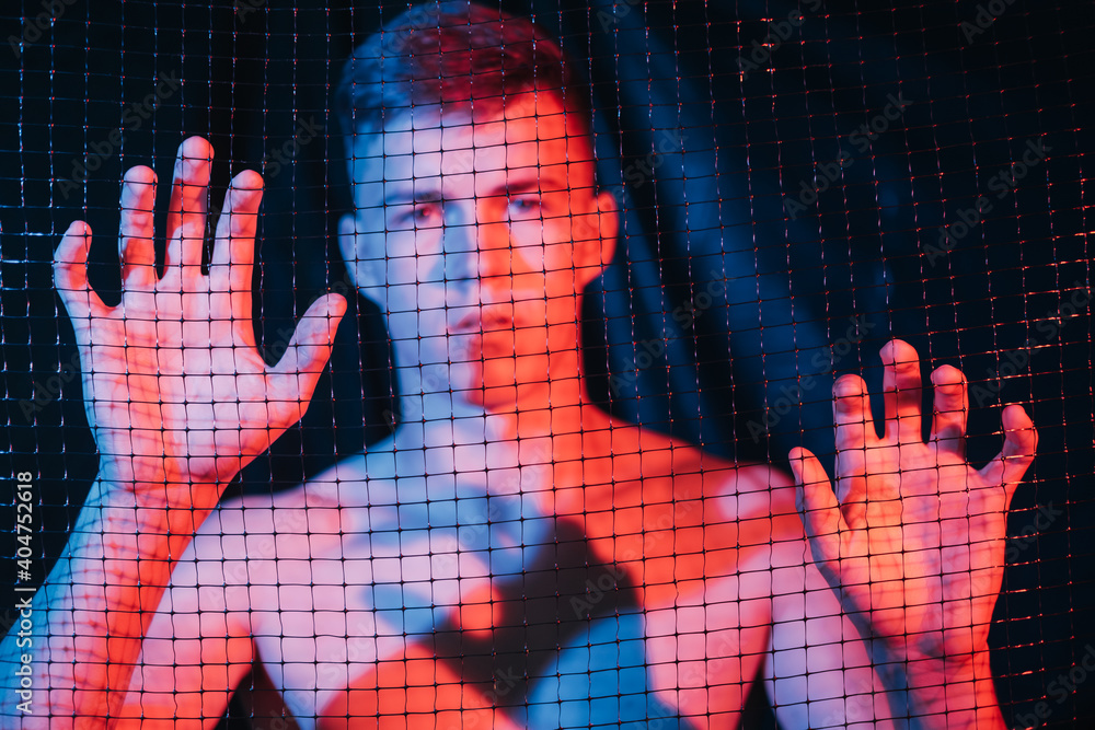 Man slavery. Defocused portrait. Human trafficking. Freedom protection.  Disturbed scared shirtless male captive trapped behind cell in red blue  neon light on blur dark background out of focus. Stock Photo | Adobe