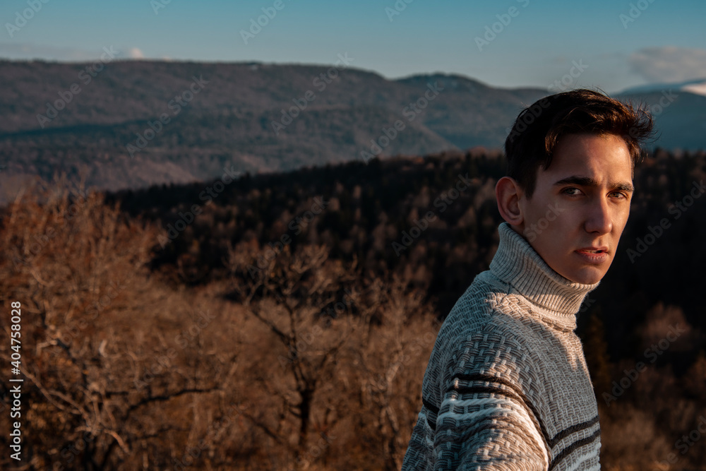 Young man in a sweater against the background of mountains. Autumn landscape. The guy is a traveler.