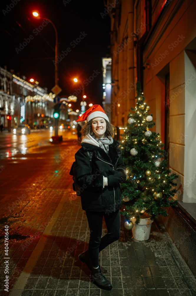 The portrait of a young girl outside in the evening dressing winter clothes and a Christmas Santa holiday hat