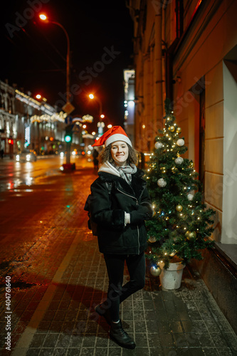 Obraz na płótnie The portrait of a young girl outside in the evening dressing winter clothes and a Christmas Santa holiday hat w salonie