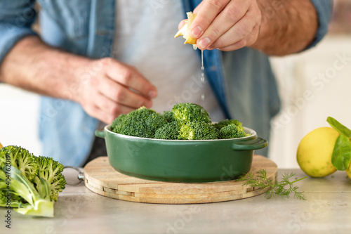 Male hands preparing healthy dinner of baked broccoli at home kitche