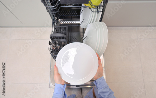 Integrated dishwaher machine. Female hand takes a clean plate from dishwasher. photo