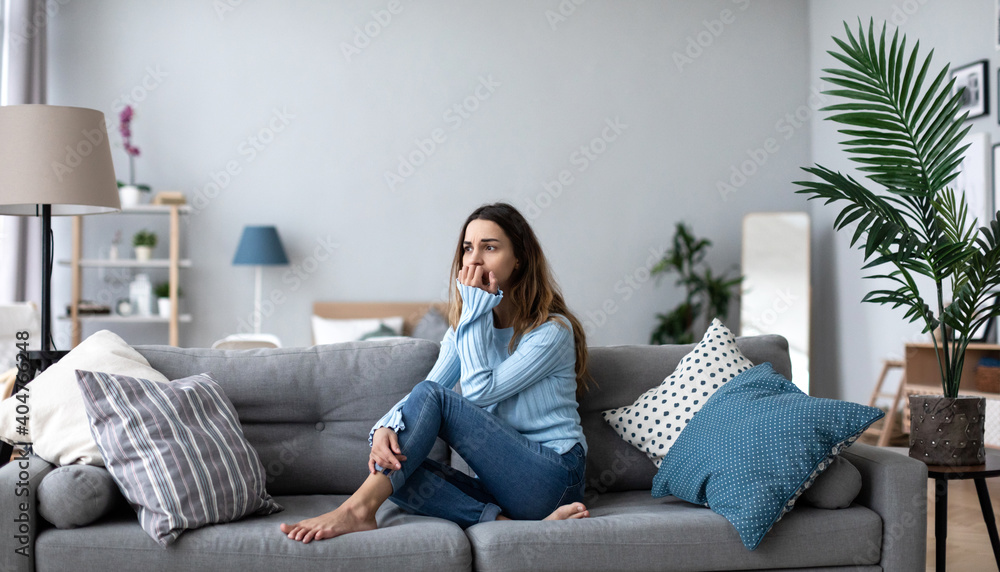 Obraz premium Upset young woman thinking about problem, sitting alone on couch at home.