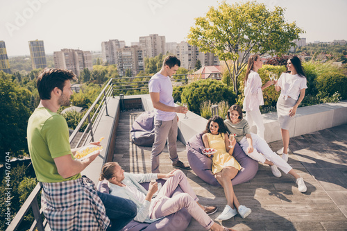 Photo of young attractive friends chill rest relax sit on beans bags chat speak drink enjoy rooftop party photo