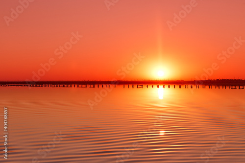 orange-red dawn on the background of a smooth lake with pillars standing in the distance (ID: 404768657)